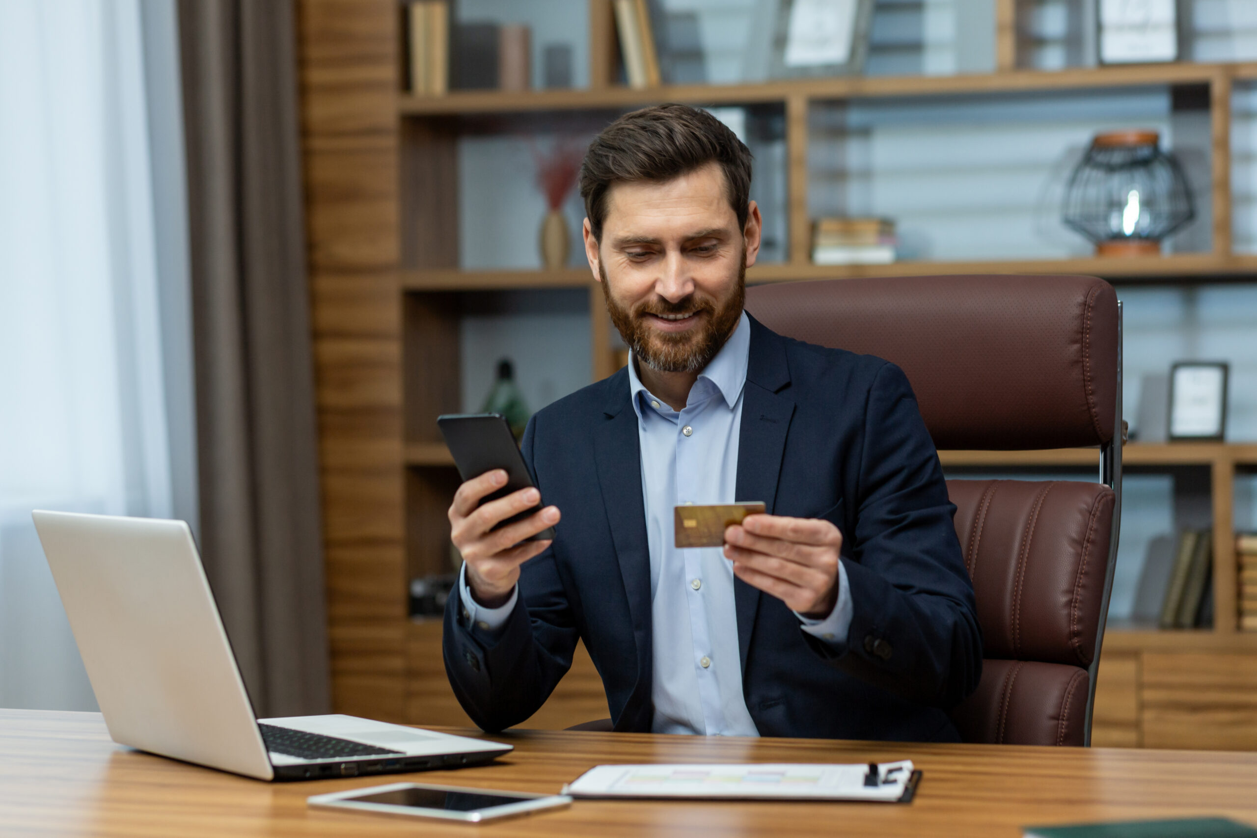 Young smiling and successful male businessman sitting in office at desk and using mobile phone and credit card Uno strumento di marketing ops per sostenere la crescita di una startup in ambito fintech